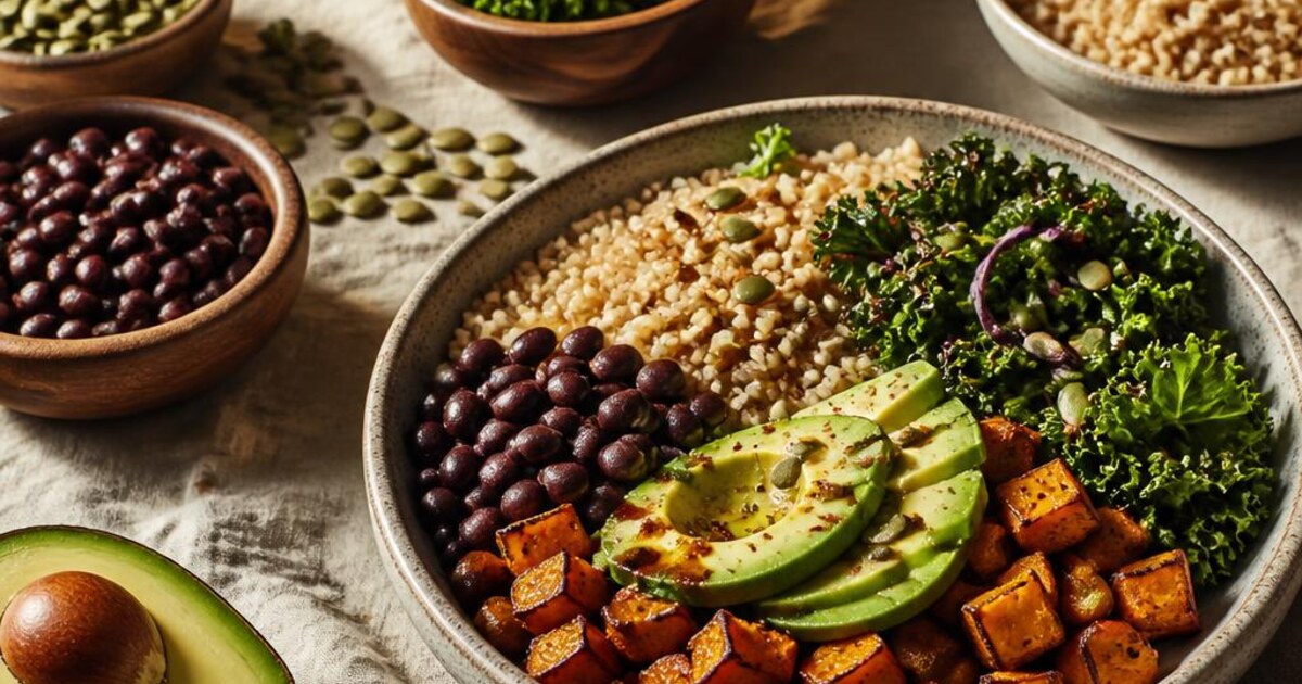 A colorful grain bowl with greens, beans, roasted vegetables and seeds on a kitchen table